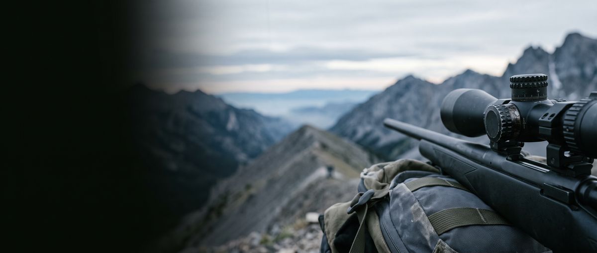Scoped hunting rifle resting on a backpack on a mountain ridge