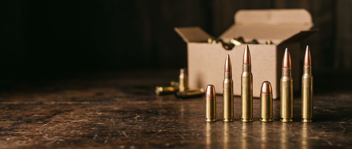 Rifle and pistol cartridges lined up in front of an open ammo box