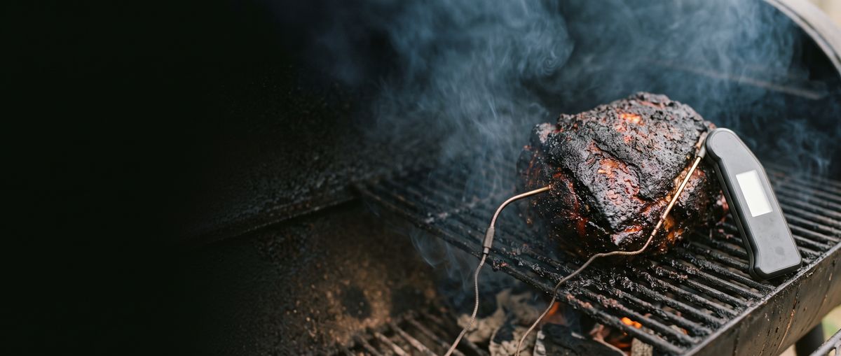 Pork shoulder with a thermometer probe on a smoking grill