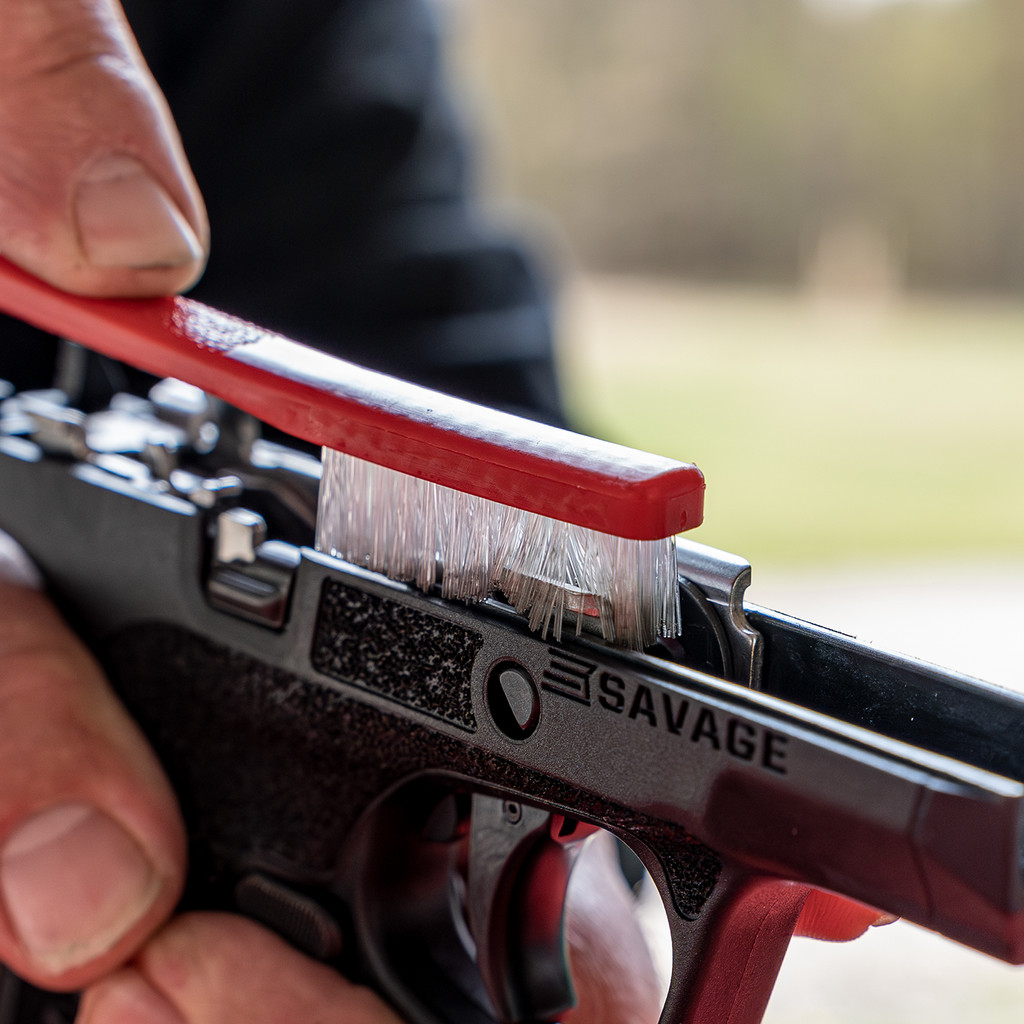 Shooters choice cleaning products - Popular Outdoorsman Close-up of a hand cleaning a Savage handgun with a red cleaning brush along the slide.