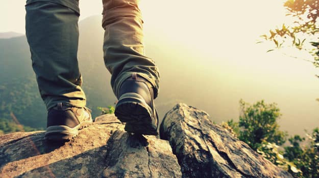 Hiker's boots on a rocky ledge at sunrise, a valley and trees in the distance.